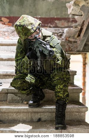 Portrait of armed woman with camouflage. Young female soldier observe with firearm. Child soldier with gun in war hearth house ruins background. Military army people concept