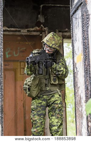 Portrait of armed woman with camouflage. Young female soldier observe with firearm. Child soldier with gun in war hearth house ruins background. Military army people concept
