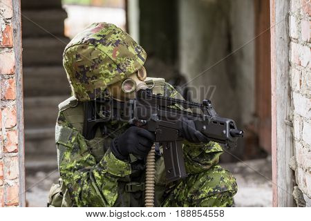 Portrait of armed woman with camouflage. Young female soldier observe with firearm. Child soldier with gun and gas mask in war hearth house ruins background. Military army people concept