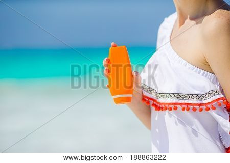 Closeup suncream bottle in female hands background turquoise water