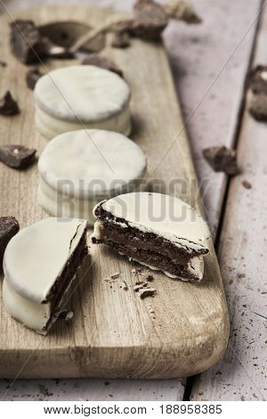some argentinean-uruguayan alfajores filled with dulce de leche and coated with a white coating on a wooden chopping board, on a rustic table