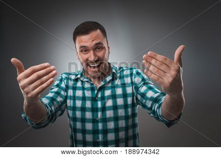 Cheerful man laughing and looking at camera with a big grin. Portrait of a happy young man standing over grey background.