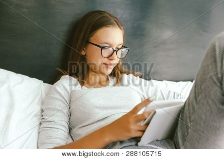 12-14 years old teenage girl using tablet pc while relaxing on couch in her room