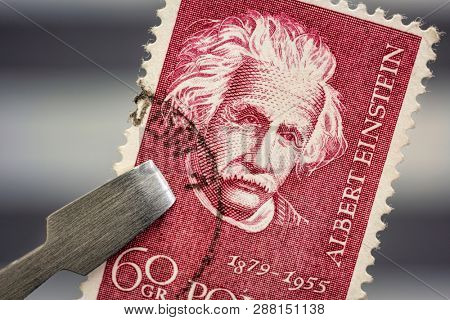 Fort Collins, CO, USA - March 6, 2019: Albert Einstein portrait on a vintage, canceled post stamp from Poland held by tweezer above a page of stamp album