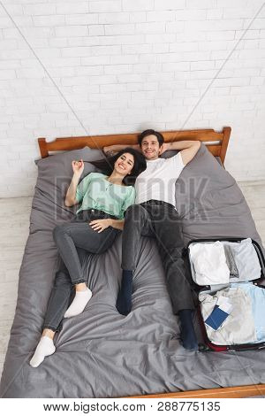 Ready For Vacasion. Young Couple Preparing For Honeymoon, Lying On Bed With Travel Suitcase