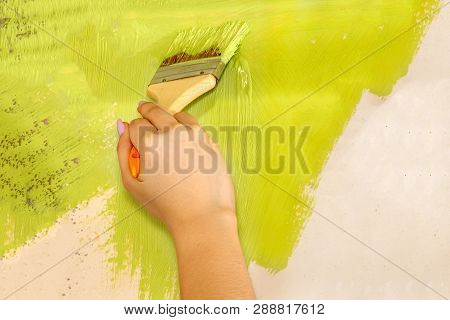Female Hand With A Flat Brush With Green Paint Paints The Wall At Home