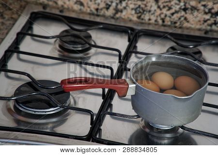 Boiled Eggs In Dipper Of Water On The Kitchen Stove.