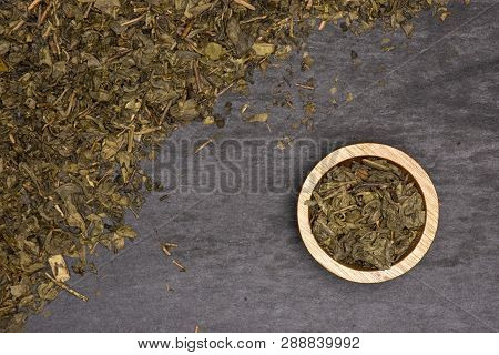 Lot Of Pieces Of Dry Green Tea With Wooden Bowl Flatlay On Grey Stone