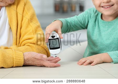 Senior Woman With Her Grandson Using Digital Glucometer At Home, Closeup. Diabetes Control