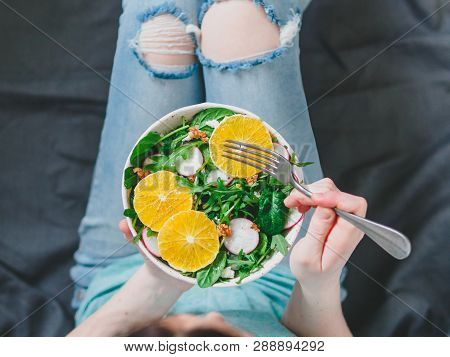 Woman In Jeans At Bed, Holding Vegan Salad Bowl With Oranges, Spinach, Arugula, Radish, Nut.top View