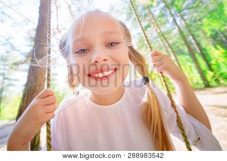 Cheerful Little Girl Swinging On A Swing Outdoors In The Forest. Close-up