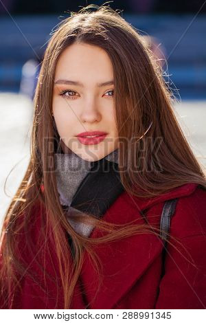 Closeup portrait of a young girl in a burgundy cashmere coat in the street