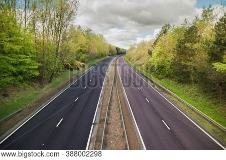 A Quiet Dual Carriage Motorway Devoid Of Traffic With Trees On Either Side And A Blue Sky Above