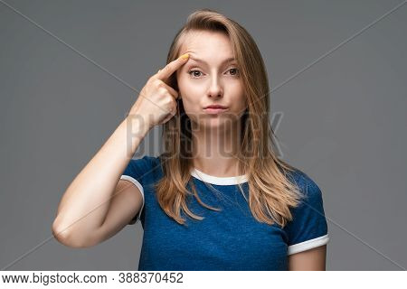 Young Female With Blonde Straight Hair And Wears Blue T Shirt Having Doubts Looks At The Camera, Her
