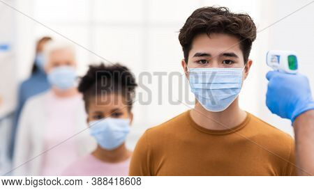 Temperature Screening. Hand With Contactless Themometer Measuring Fever, Scanning Forehead Of Chines