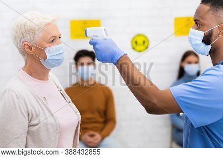 Nurse Doing Temperature Screening Measuring Fever For Senior Lady Patient Before Doctors Appointment