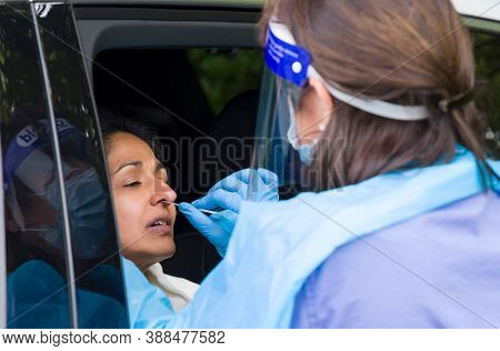 Asian Woman In A Car Having A Coronavirus Nasal Swab Test With A Nurse In Ppe Gear. England, Uk