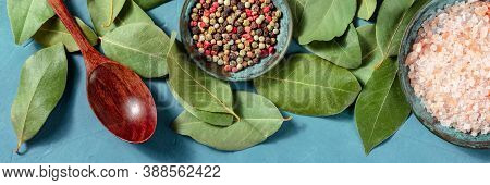 Culinary Panorama With Salt, Pepper, Bay Leaves, And A Wooden Spoon, Top Shot On A Blue Background