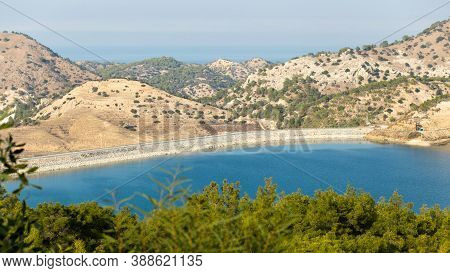 Reservoir In The Mountains. Sunny Bright Day. Top View Of The Reservoir, The Foreground Is Blurred.