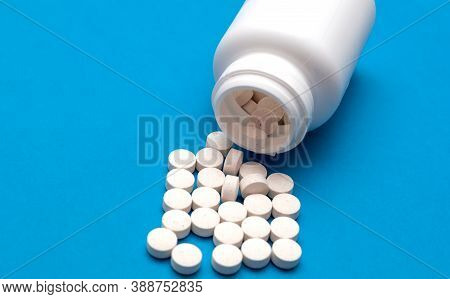 White Pills Scattered From A White Bottle, Jar On A Blue Background. Health Care And Treatment Conce