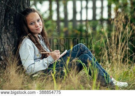 Teengirl writing in a notebook while sitting in the park.