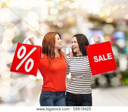 shopping, sale, mall and gift sconcept - two smiling teenage girls with shopping bags and percent sign at shopping mall