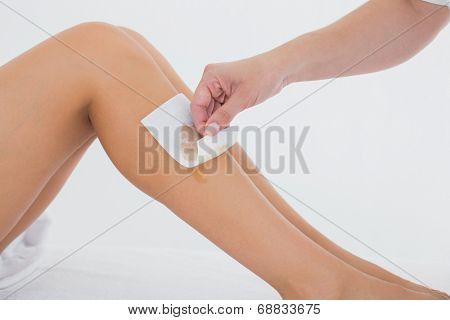 Mid section of therapist waxing woman's leg at spa center