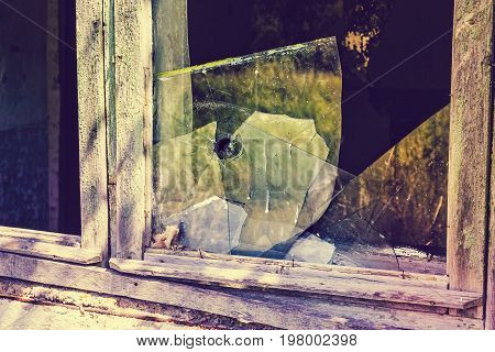 Broken window with broken glass. Bullet hole in the glass, toned