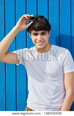 Young Man Happy Man Holding Sunglasses Against Blue Wooden Wall