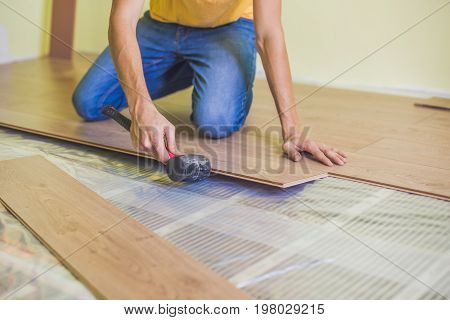 Man Installing New Wooden Laminate Flooring. Infrared Floor Heating System Under Laminate Floor