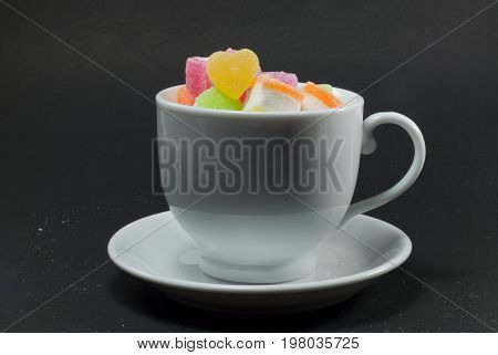 Multicolored jelly in a white cup against a black background.