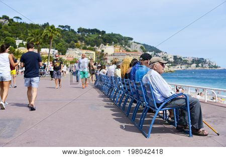 NICE, FRANCE - JUNE 4, 2017: People at the famous Promenade des Anglais walking and sitting in the characteristic blue chairs facing the Mediterranean sea in Nice, in the French Riviera, France