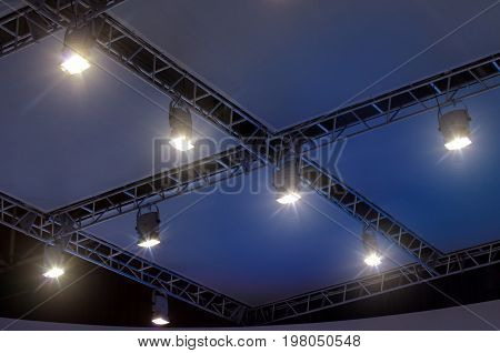 A row of four light projectors on a scene ceiling with cables and metal supports