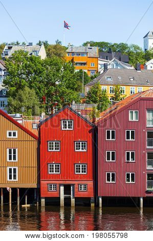 Famous wooden colored houses in Trondheim city Norway. Colorful houses on stilts and flag of Norway in sunny day.