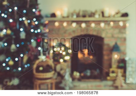 Abstract blurred background of Christmas setting, decorated lounge, firepalce with woodburner, lit up Christmas tree with baubles and ornaments, lantern, stars and garlands, selective focus, toned