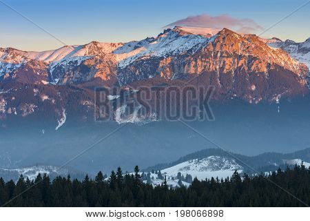 Fantastic view in winter season with the peak of Bucegi massif in the warm colorful sunset light landscape seen from resort Fundata Cheile Gradistei Romania.