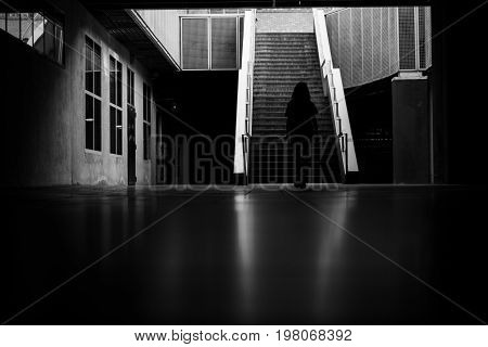 Black and white photograph of a black silhouette of a girl walking towards a few stairs in the city.