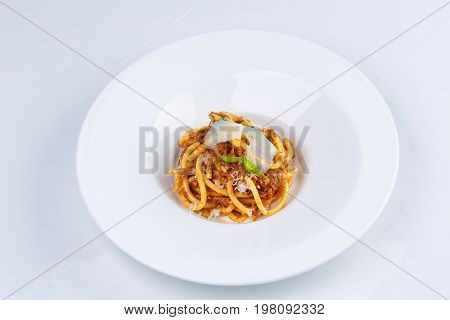 Pasta with tomato sauce and parmesan in white plate on white tablecloth.