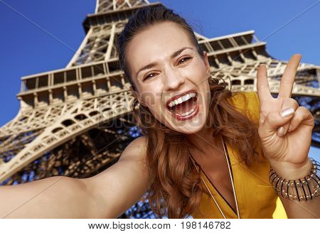 Woman Taking Selfie And Showing Victory Against Eiffel Tower