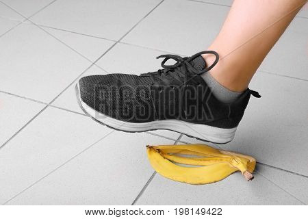 Male's leg in black trainers slips on a banana peel, on a gray background. Bright yellow banana peel on the floor. Accident, danger and risk concept.