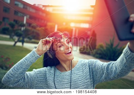 Woman taking selfie with tablet in park making expression in sunset