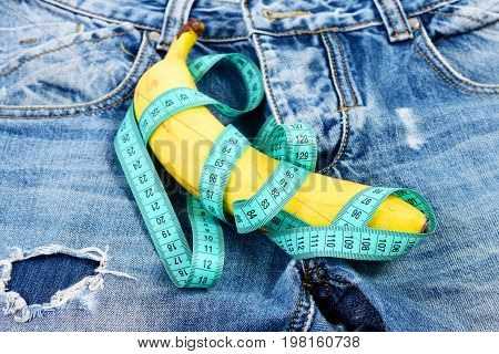 Jeans zipper and pocket close up. Mens denim pants crotch with banana imitating male genitals. Health and male sexuality concept. Banana wrapped with blue measure tape on jeans selective focus.