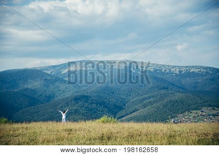 woman in field with mountains on background pictered from long distance in summer day