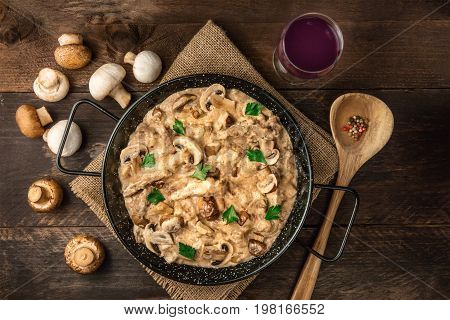 Mushroom beef stroganoff, with cremini and champignons, in a frying pan, shot from above on a dark rustic texture with a place for text and a glass of red wine