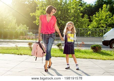 Mom and schoolgirl of primary school holding hands. The parent takes the child to school. Outdoors return to the concept of the school