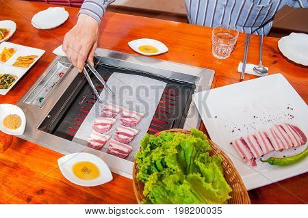 Process Of Cooking Korean Barbecue Raw Pork On The Tabletop Grill In Restaurant. Selective Focus. Cl