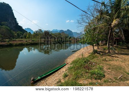 Beautiful landscape picture of the Nam Song River with tropical vegetation and two boats. Close to Tham Chang Cave in the city of Vang Vieng Laos.