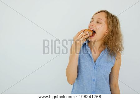 Closeup portrait of young attractive woman holding cake and biting it with her eyes closed. Isolated front view on grey background.