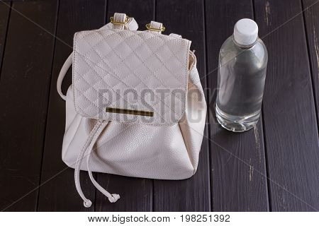 White leather backpack and water bottle on a black wooden background