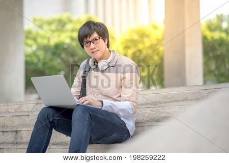 Young Asian man sitting on stair and working with laptop in college building university student or high school lifestyle. education concept